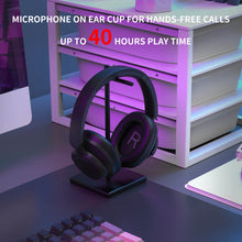 Black headphones on a stand with promotional text about microphone on ear cup and play time on a desk setup.