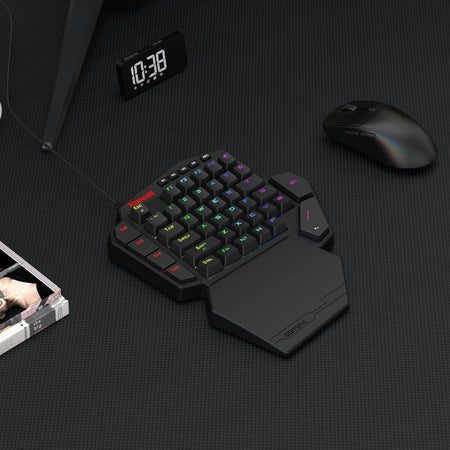 Black ergonomic keyboard with RGB backlighting on a dark surface, next to a mouse and digital clock.