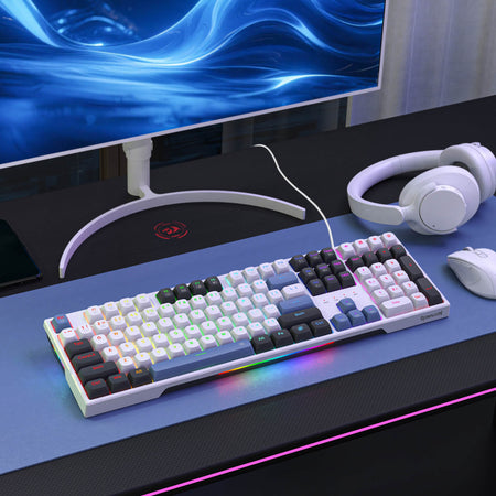 Mechanical keyboard on a desk with a monitor, headphones, and mouse in the background