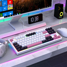 Colorful keyboard on a desk with a computer monitor, speakers, and clock in the background.